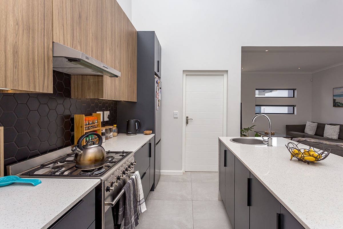 Modern kitchen featuring a central island with sink, gas stove, stone countertops, and sleek two-tone cabinetry with a stylish hexagonal tile backsplash.