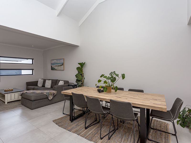 Spacious open-plan living and dining area featuring high vaulted ceilings, neutral tiled flooring, and modern horizontal windows providing natural light.