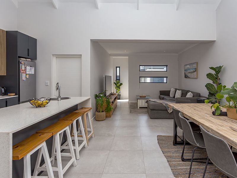 Modern open-plan living area featuring a sleek kitchen with stone island, tiled floors, and high vaulted ceilings, creating a bright and spacious atmosphere.
