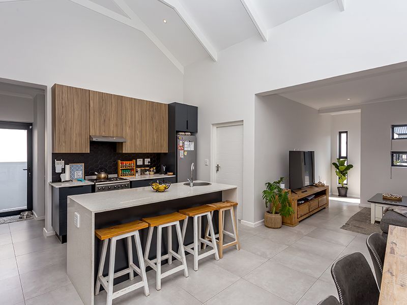 Modern open-plan kitchen and living area featuring a vaulted ceiling, sleek cabinetry, a central island with sink, and contemporary tiled flooring.