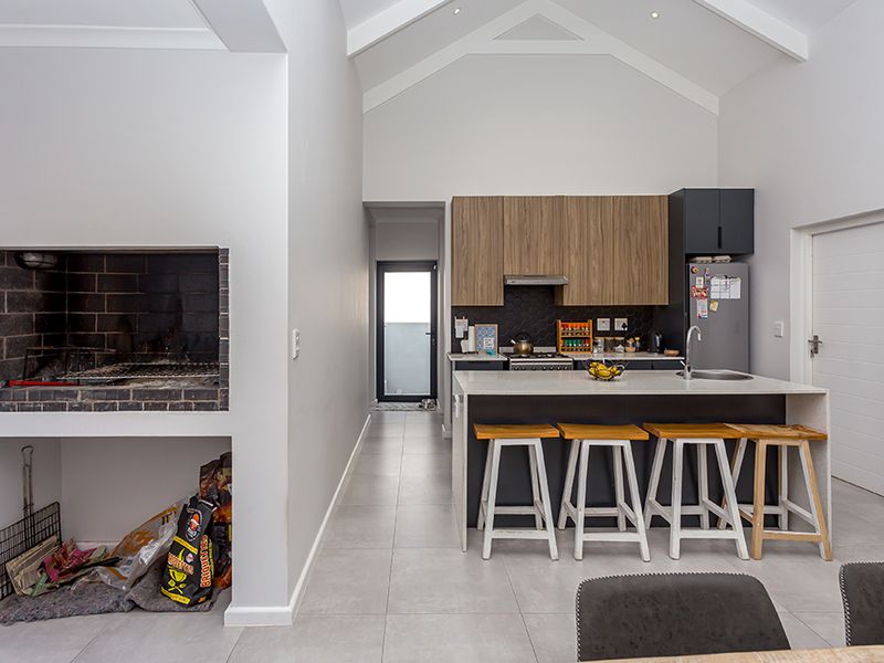 Open-plan kitchen featuring modern cabinetry, a central island, and a built-in indoor braai area under a high vaulted ceiling.