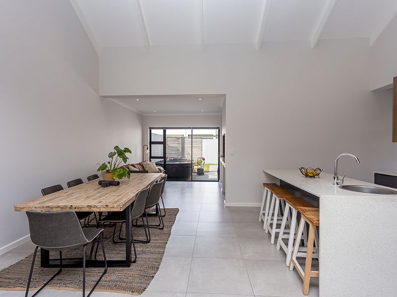 Modern open-plan living and dining area featuring a sleek kitchen island with stone countertops, vaulted ceilings, and seamless access to the rear patio.