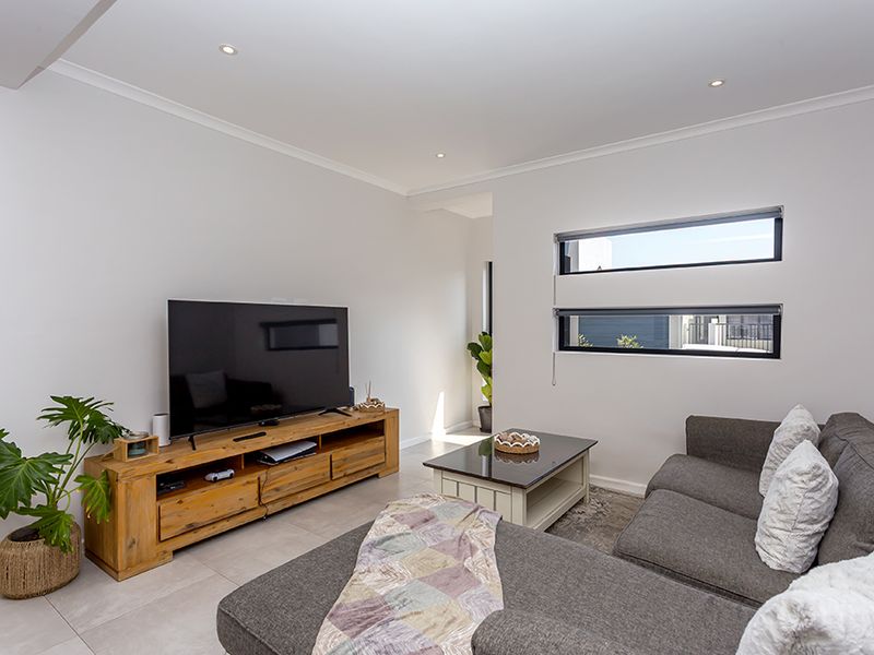 A bright and modern living room featuring neutral tiled flooring, recessed downlighting, and horizontal windows that provide natural light.