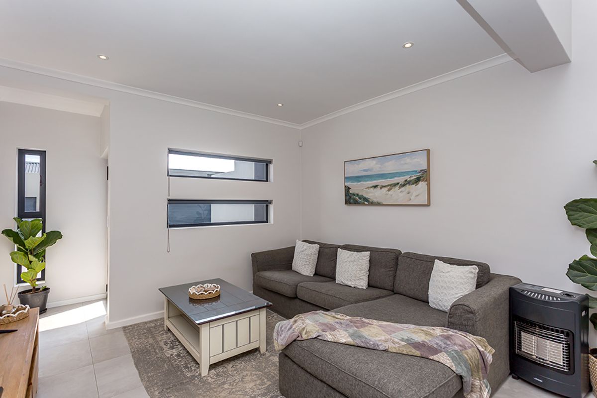 A bright and modern living room featuring neutral walls, tiled flooring, recessed downlighting, and horizontal windows that provide natural light.