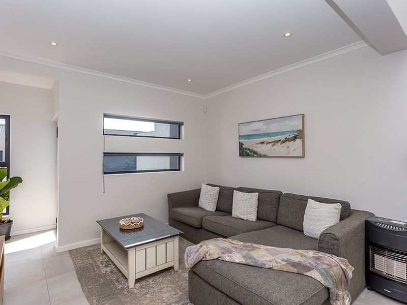 A bright and modern living room featuring neutral walls, tiled flooring, recessed downlighting, and horizontal windows that provide natural light.