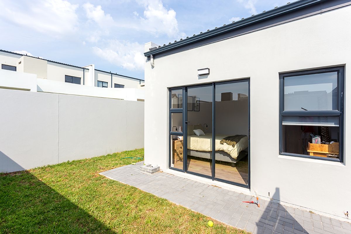Rear view of the property featuring a paved patio area, sliding glass doors leading into the bedroom, and a private garden with boundary walls.