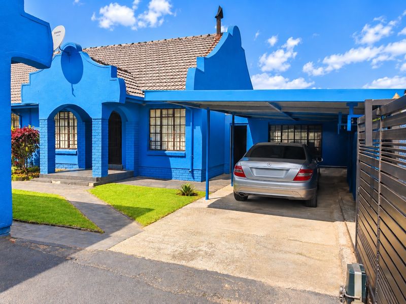 Front view of a blue-painted house featuring a tiled roof, a covered carport, and a paved driveway with a gated entrance.