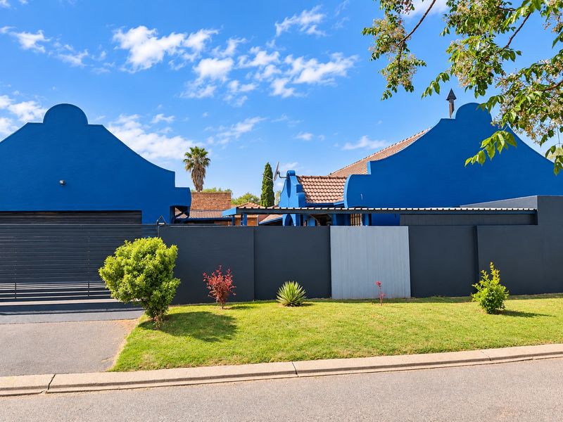 Front elevation of a house featuring distinctive blue gabled facades, a dark boundary wall, and a paved driveway.