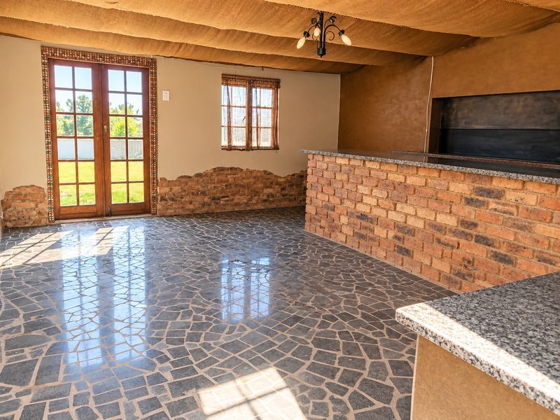 Spacious entertainment area featuring a built-in brick bar with granite countertop, built-in braai, stone mosaic flooring, and direct access to the garden.