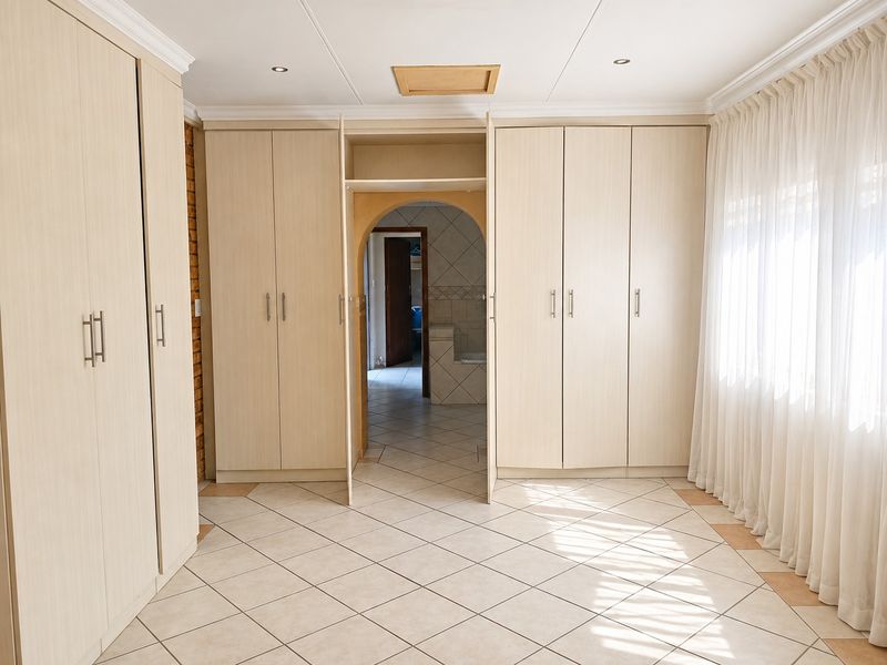 Spacious bedroom featuring extensive built-in cabinetry, neutral tiled flooring, and an arched entryway leading to an adjoining space.