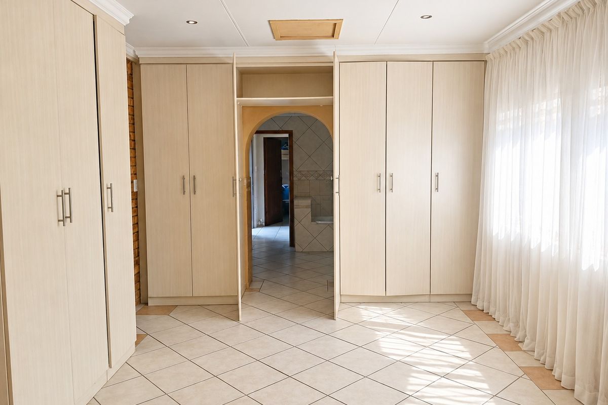 Spacious bedroom featuring extensive built-in cabinetry, neutral tiled flooring, and an arched entryway leading to an adjoining space.