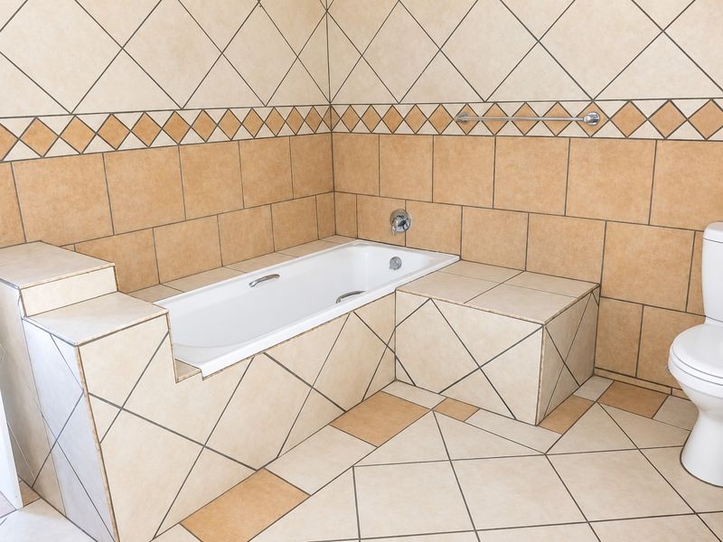A functional bathroom featuring a built-in bathtub with tiled surround, ceramic wall and floor tiles, and a standard toilet.