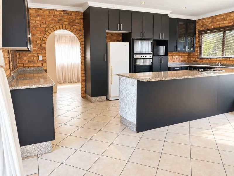 Spacious kitchen featuring dark cabinetry, granite countertops, a built-in oven, and a distinctive brick feature wall with an arched entryway.