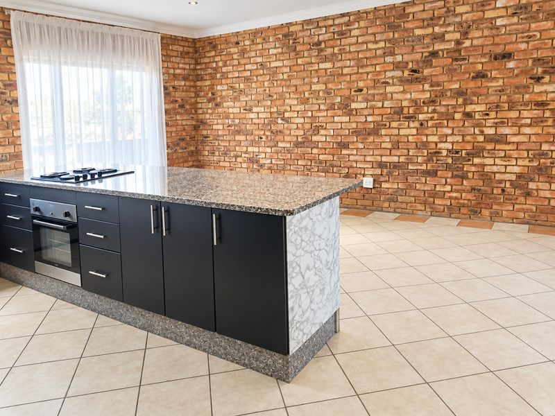 Modern kitchen island featuring a granite countertop, built-in oven, and gas hob, set against a characterful exposed brick wall and neutral tiled flooring.