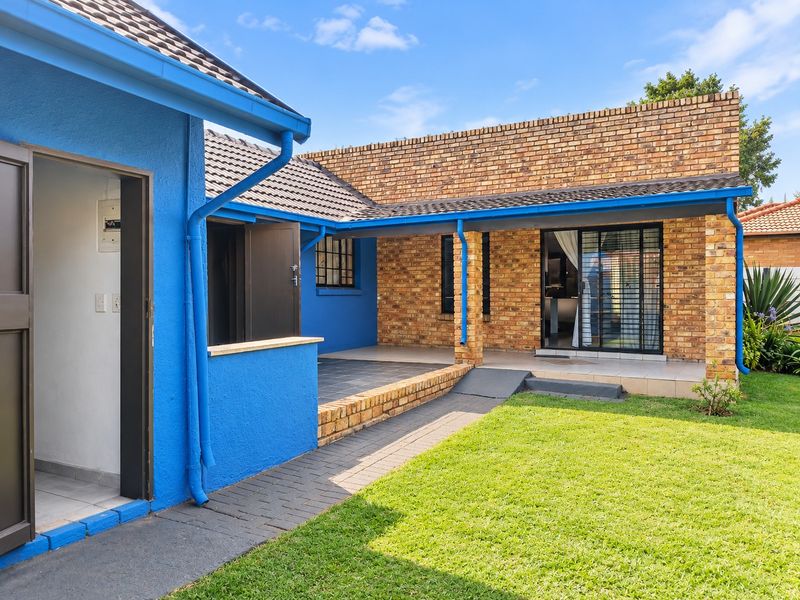Rear exterior view featuring a covered patio, brick and painted blue facade, paved walkway, and well-maintained lawn area.