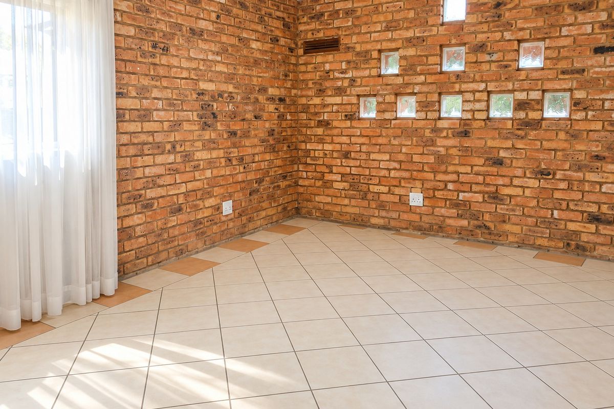 An empty living area featuring exposed brick walls, decorative glass block inserts, and neutral ceramic floor tiles, offering a versatile space for interior design.