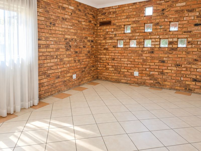 An empty living area featuring exposed brick walls, decorative glass block inserts, and neutral ceramic floor tiles, offering a versatile space for interior design.