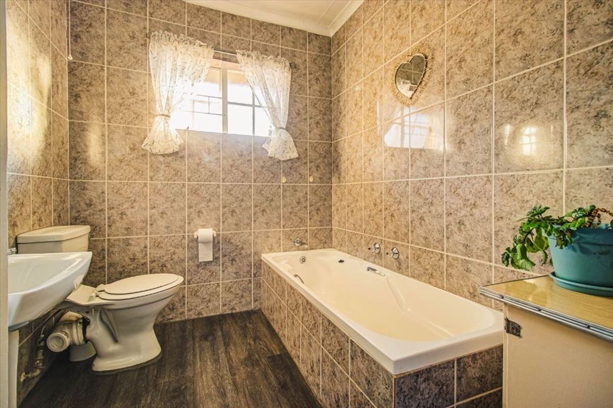 A functional bathroom featuring full-height wall tiling, a built-in bathtub, a pedestal basin, and a toilet with wood-look laminate flooring.