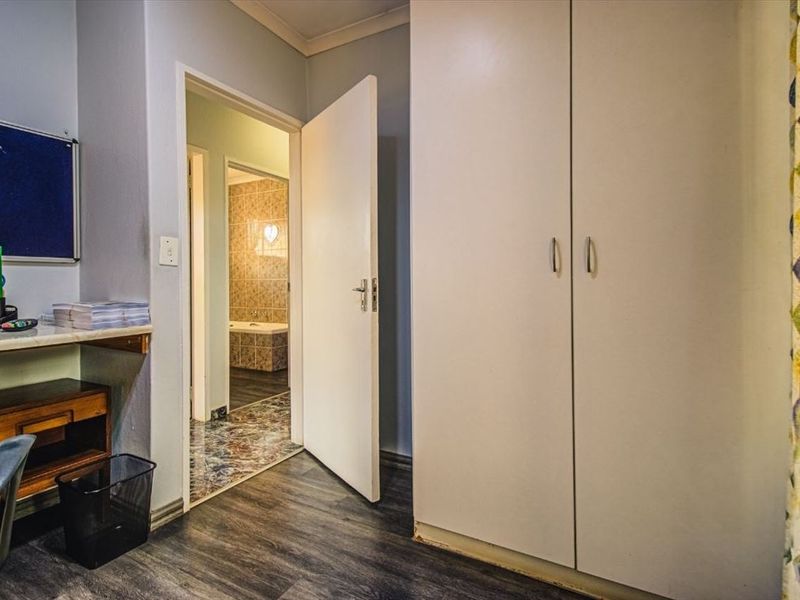 Bedroom featuring built-in cupboards, laminate flooring, and a built-in desk, with an adjoining bathroom visible through the doorway.