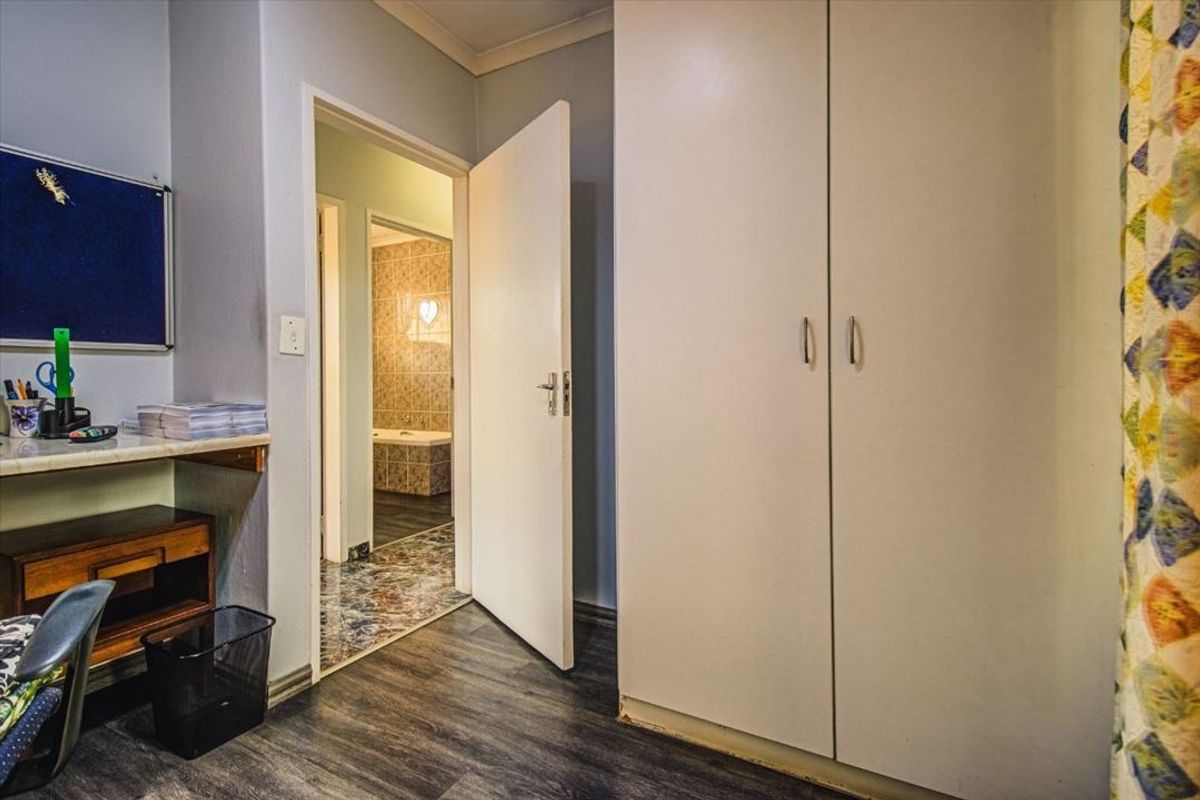 Bedroom featuring built-in cupboards, laminate flooring, and a built-in desk, with an adjoining bathroom visible through the doorway.