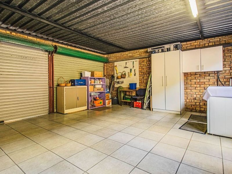 A functional garage space featuring tiled flooring, exposed brick walls, corrugated metal ceiling, and built-in storage cabinetry.