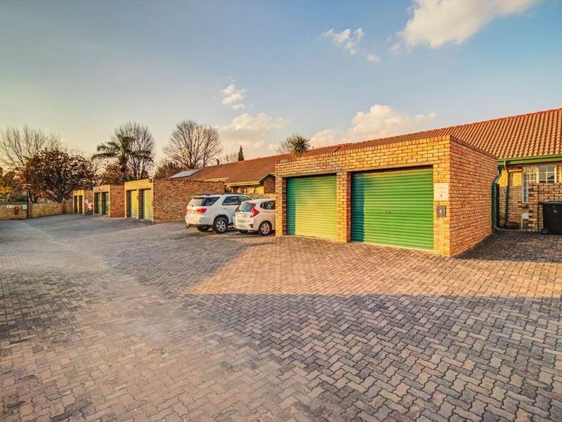 Exterior view of a row of brick garages with green roller shutter doors and a paved driveway area.