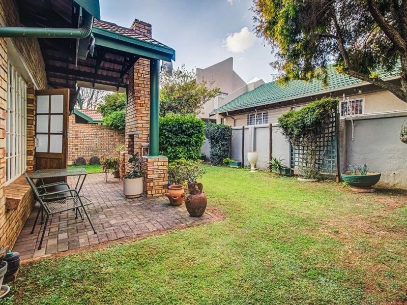 A private rear garden featuring a paved patio area with a built-in brick braai, lawn, and perimeter walling.