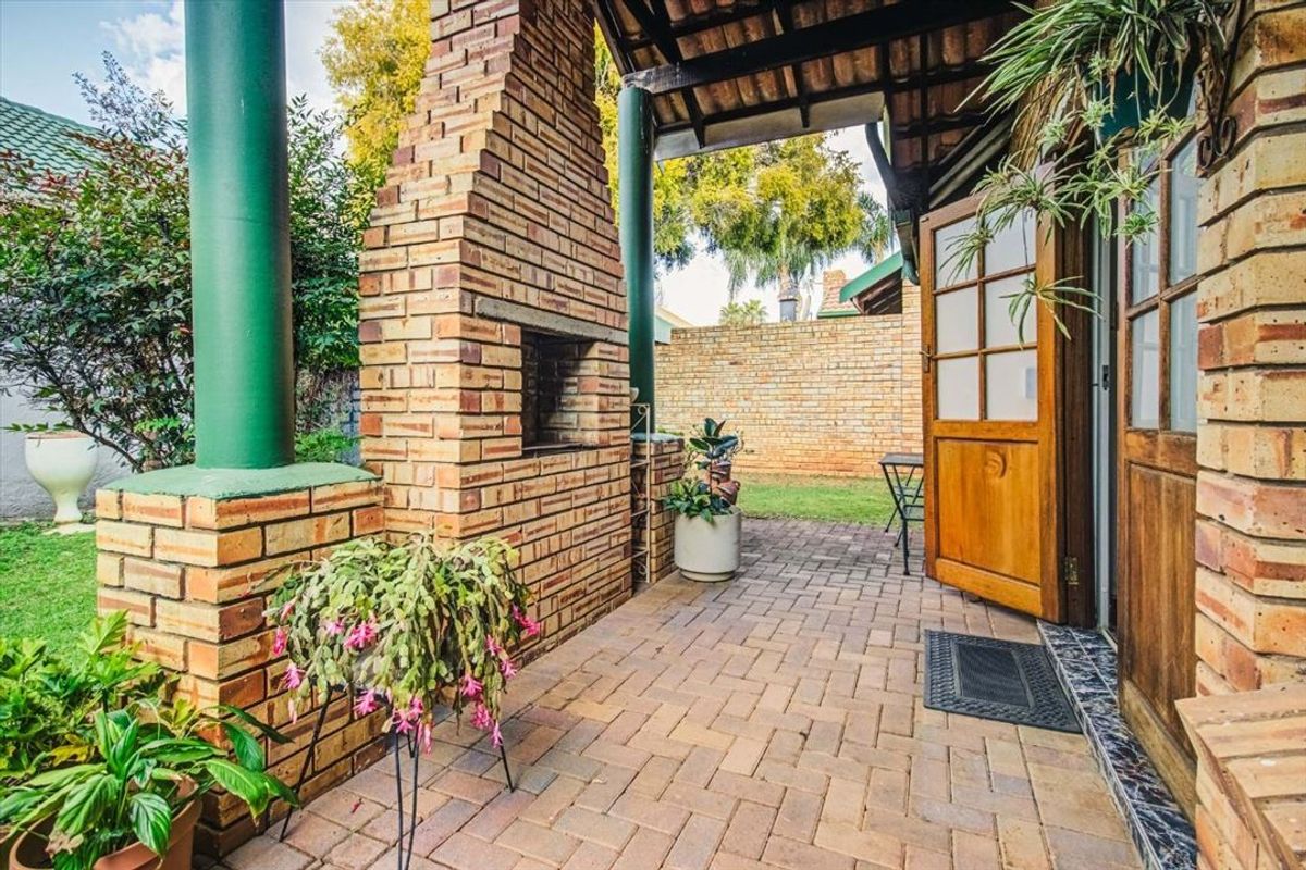A covered patio area featuring a built-in brick braai, brick paving, and direct access to the garden through timber doors.