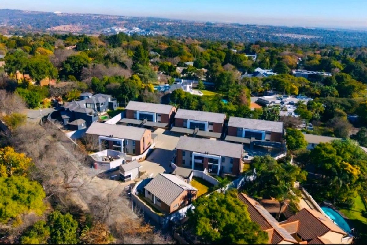 Aerial view of a residential apartment complex featuring multiple buildings with tiled roofs and paved driveway access within a landscaped suburban setting.