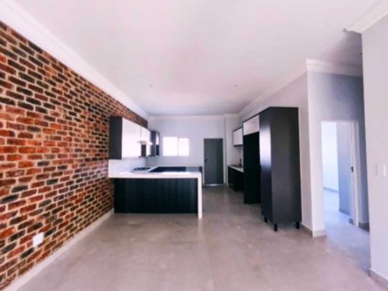 Modern open-plan kitchen and living area featuring an exposed brick feature wall, sleek built-in cabinetry, and neutral tiled flooring.