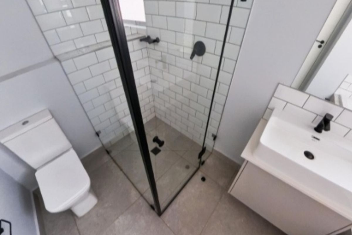 Modern bathroom featuring a glass-enclosed shower with subway tiles, a vanity with a basin, and a toilet, all finished with contemporary black fixtures.