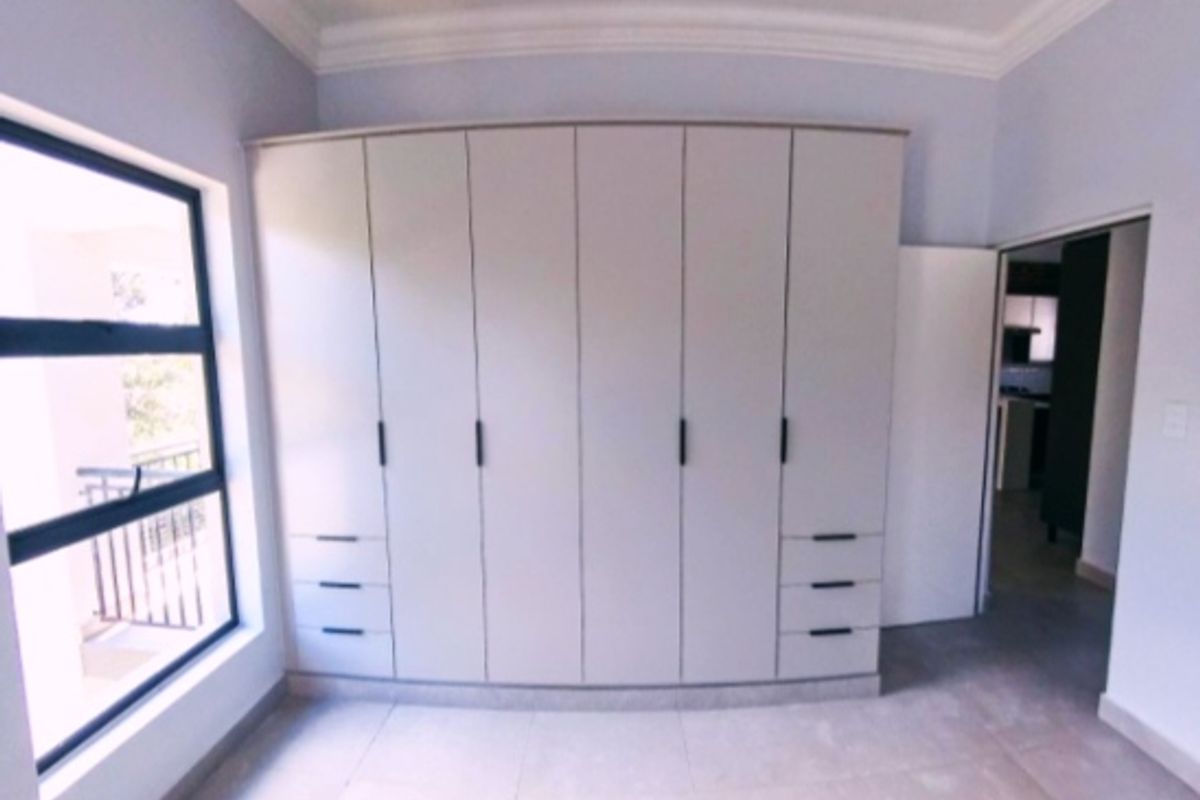 A bright, empty bedroom featuring modern built-in cupboards, tiled flooring, and a large window providing natural light.
