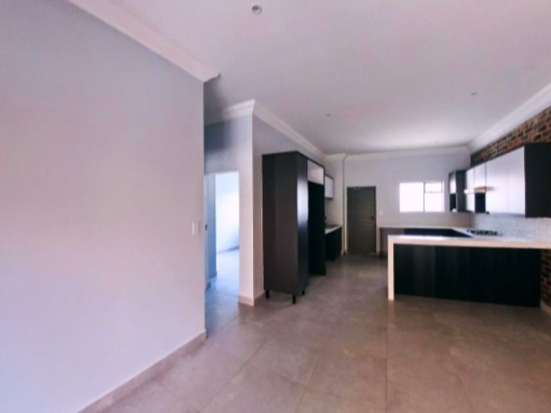 Spacious open-plan living and kitchen area featuring modern dark cabinetry, a kitchen island, tiled floors, and an exposed brick feature wall.