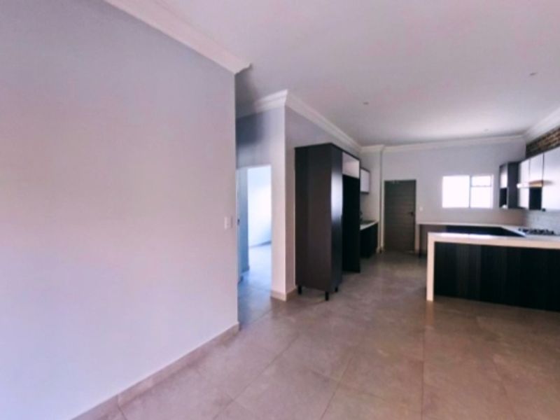 Spacious open-plan living area featuring modern dark cabinetry, a kitchen island, tiled flooring, and neutral wall finishes.