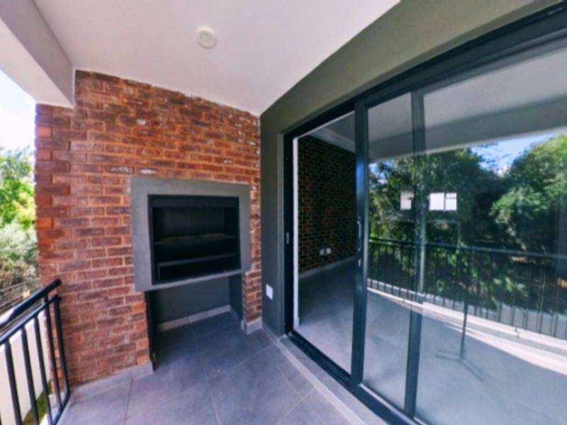 A modern covered balcony featuring a built-in braai, tiled flooring, and large sliding glass doors providing seamless access to the interior living space.