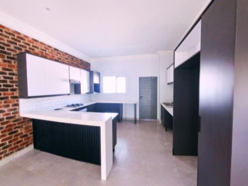 Modern kitchen featuring an exposed brick feature wall, sleek built-in cabinetry, a central island with stone countertops, and integrated cooking appliances.
