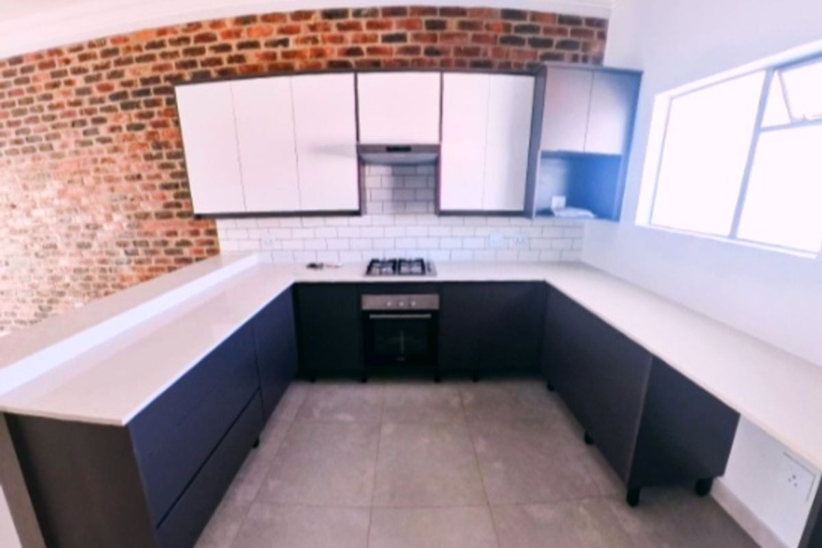Modern kitchen featuring dark cabinetry, stone countertops, gas hob, electric oven, and a stylish exposed brick feature wall.