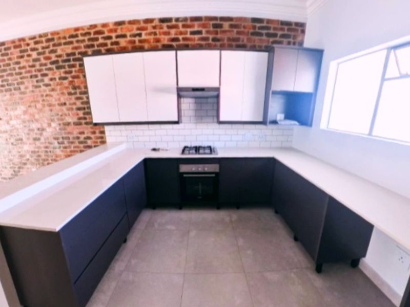 Modern kitchen featuring dark cabinetry, stone countertops, gas hob, electric oven, and a stylish exposed brick feature wall.