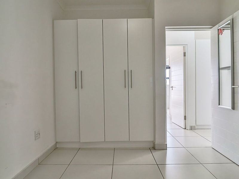 A clean, empty bedroom featuring white built-in cupboards, tiled flooring, and neutral finishes, offering a bright and versatile space.