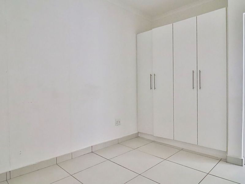 A clean, empty bedroom featuring white built-in cupboards, neutral tiled flooring, and bright, minimalist finishes.