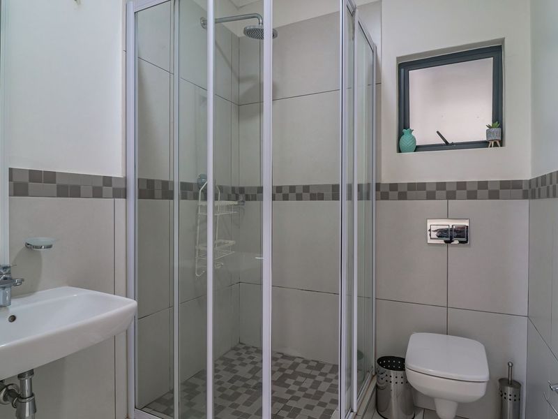 A clean, modern bathroom featuring a glass shower enclosure, wall-hung toilet, and a wall-mounted basin with neutral tiling.