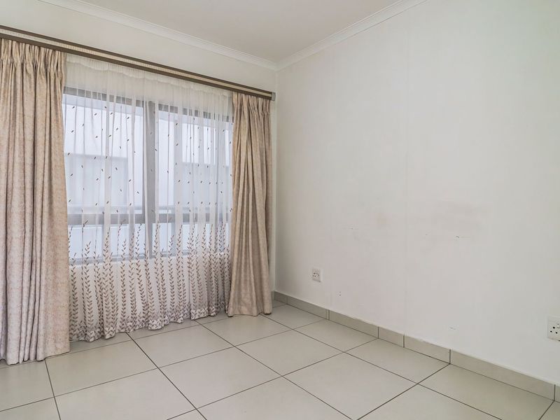 An empty bedroom featuring neutral tiled flooring, white walls with minor scuffing, and a window fitted with a curtain rail.