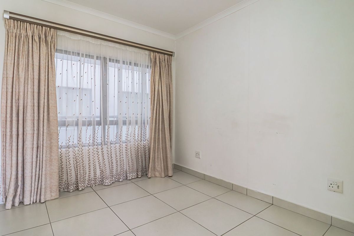 An empty bedroom featuring neutral tiled flooring, white walls with minor scuffing, and a window fitted with a curtain rail.