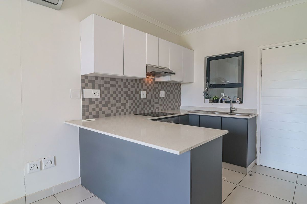 Modern kitchen featuring white and grey cabinetry, quartz countertops, mosaic backsplash, electric hob, and tiled flooring in a clean, functional layout.