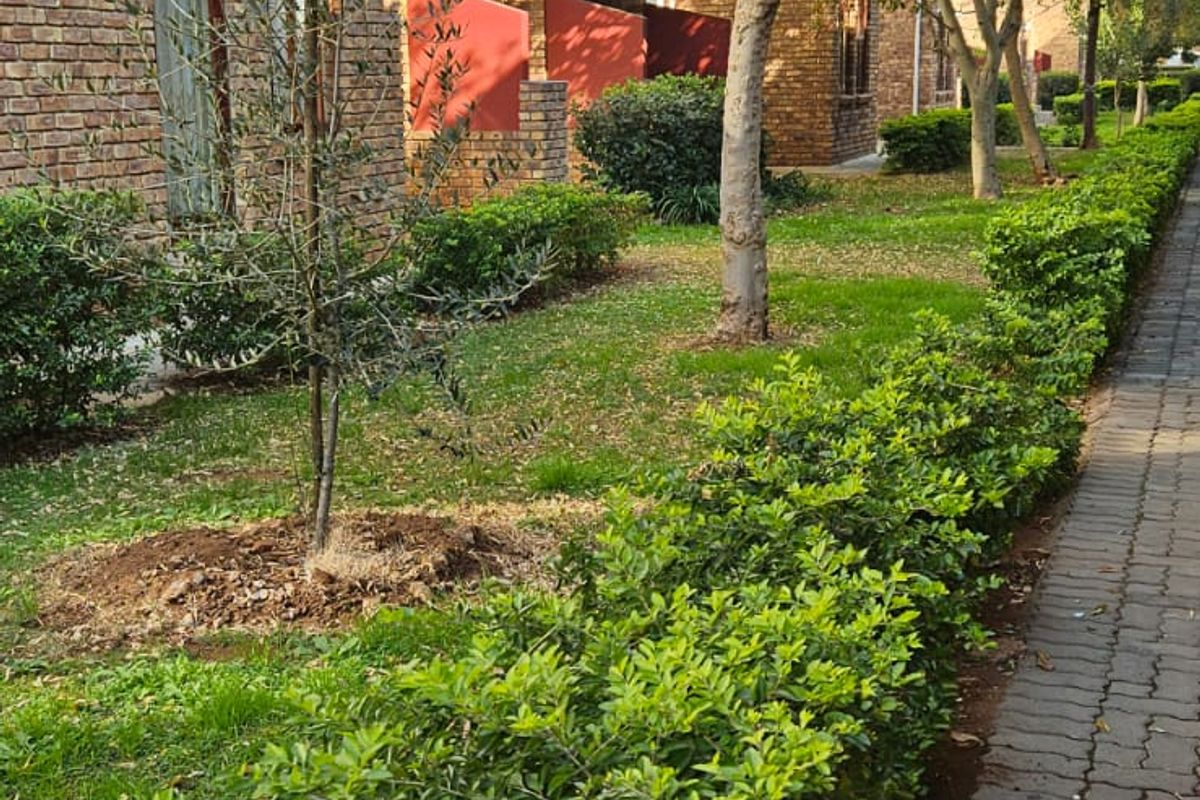 A well-maintained exterior view of the apartment complex featuring a brick facade, manicured garden hedges, and a paved walkway.