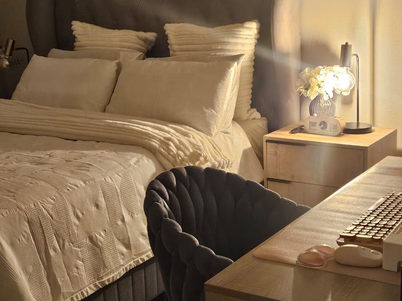 A cozy bedroom featuring a tufted headboard and a dedicated workspace area with warm ambient lighting.