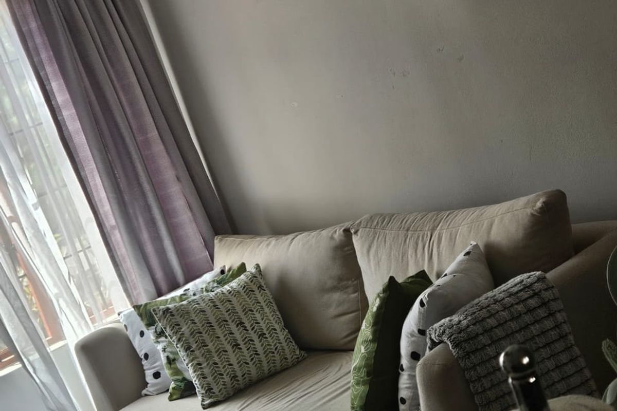 A cozy living room area featuring neutral wall tones, tiled flooring, and natural light through window treatments.