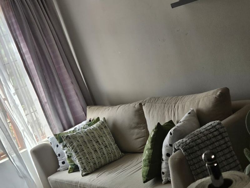 A cozy living room area featuring neutral wall tones, tiled flooring, and natural light through window treatments.