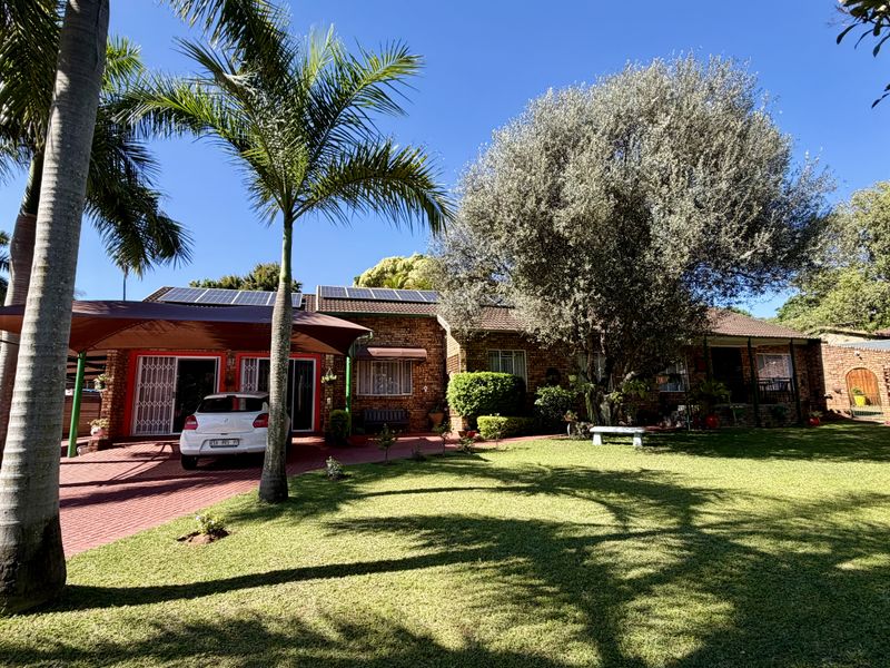 Front view of a brick house featuring a paved driveway, carport, solar panels, and a well-maintained garden with mature trees.