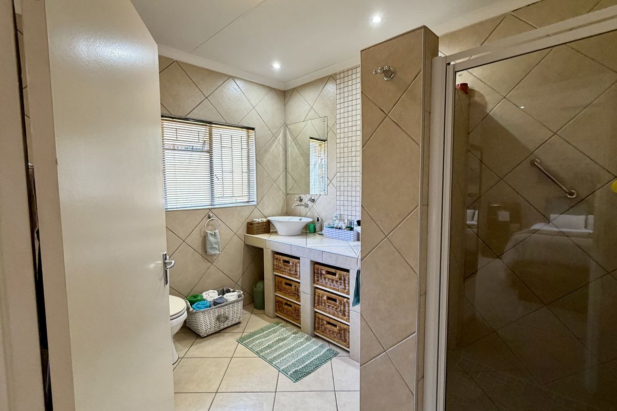 A functional bathroom featuring a tiled vanity with a vessel sink, a separate shower enclosure with a grab rail, and neutral wall and floor tiling.
